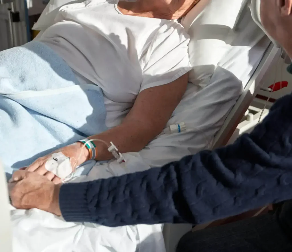 Frau hält Hand von Senior im Krankenhaus Bett