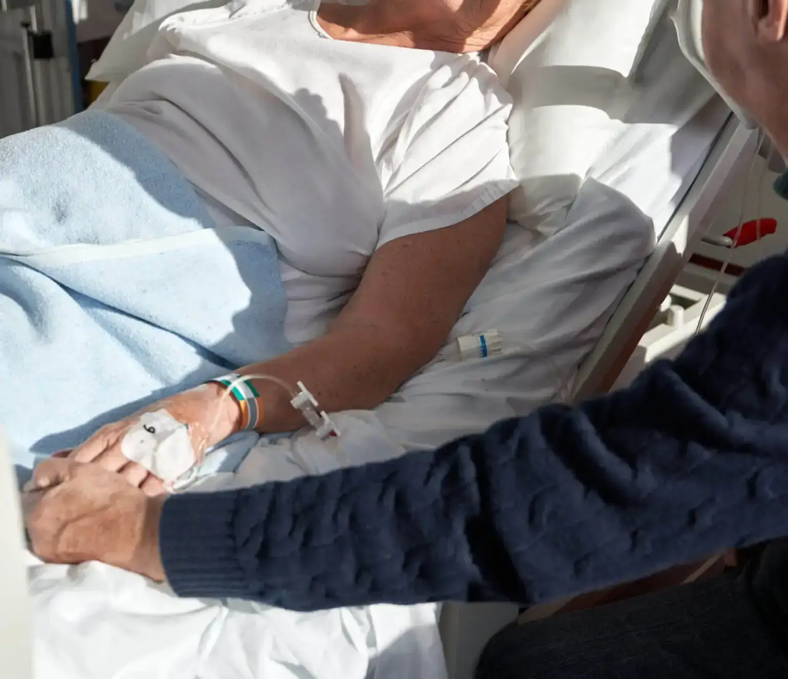 Frau hält Hand von Senior im Krankenhaus Bett